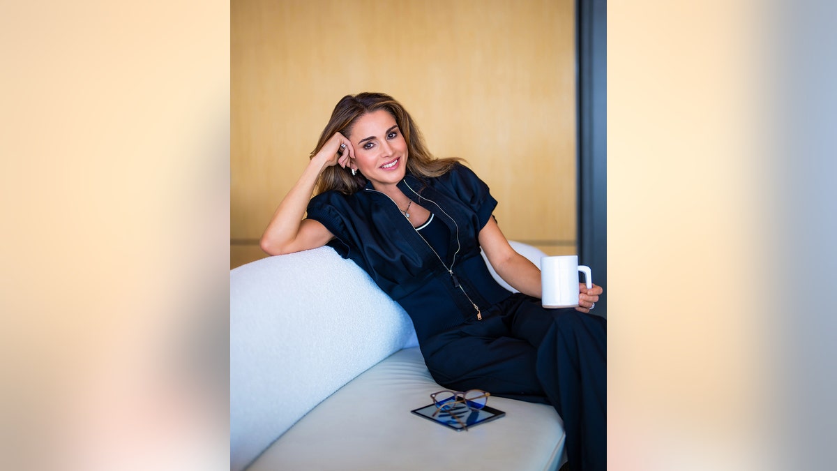 Queen Rania of Jordan wearing a dark suit and holding a white mug