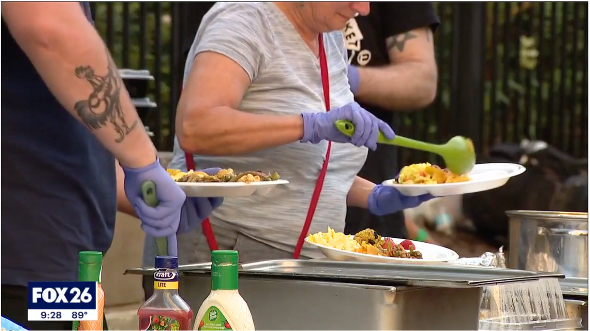 A volunteer can be seen scoops food into a plate outside the Houston Public Library downtown