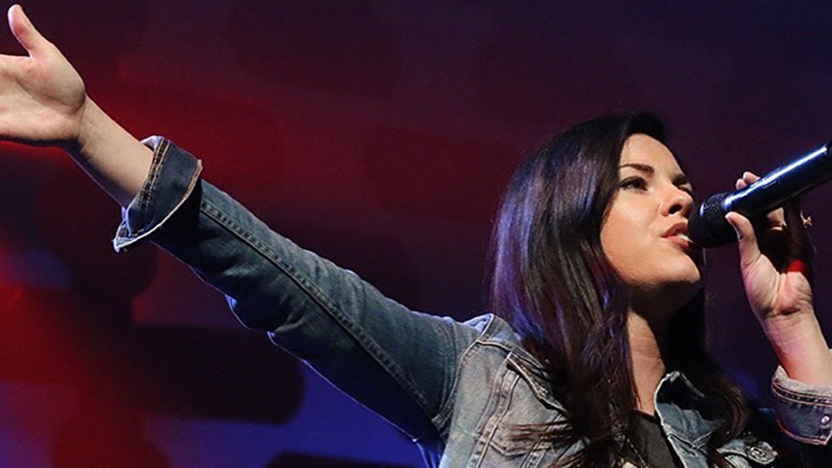 A close-up of Tasha Layton wearing a denim jacket and singing to a mic.