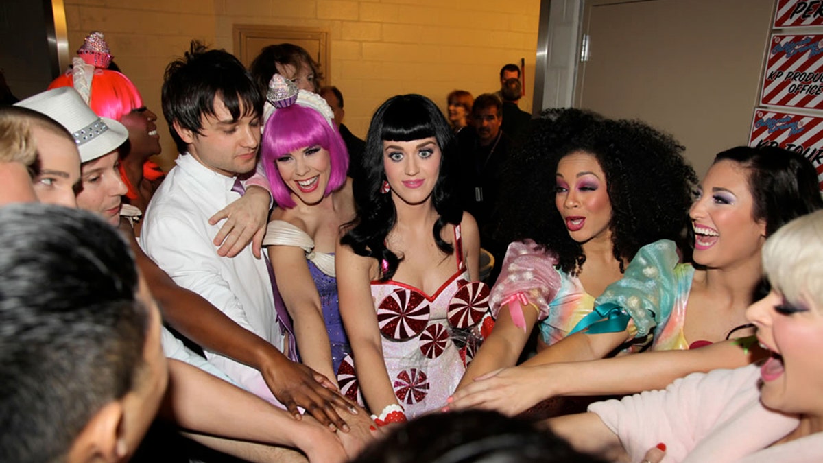 Katy Perry and her crew gathered together backstage in a huddle. Tasha Layton is wearing a hot pink bob wig.