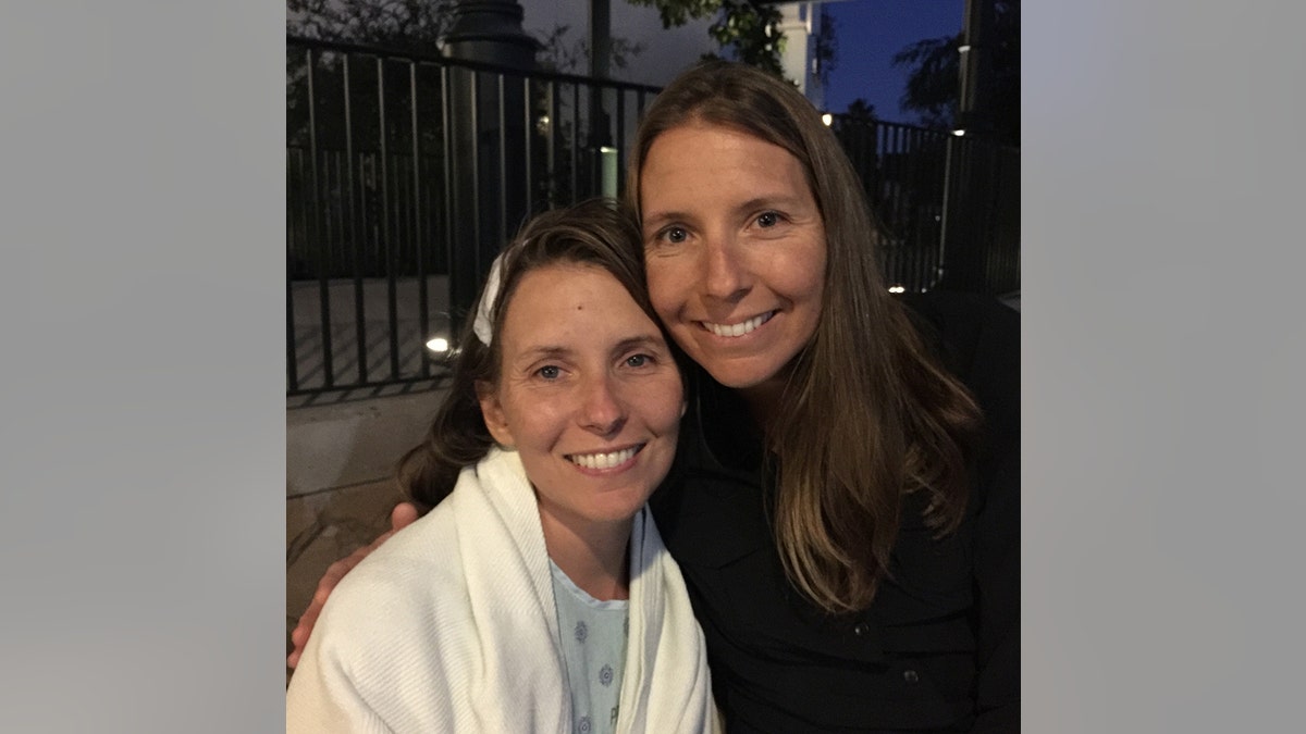 Wendi Lou Lee in a white robe and light blue shirt posing with her twin sister in a black turleneck sweater