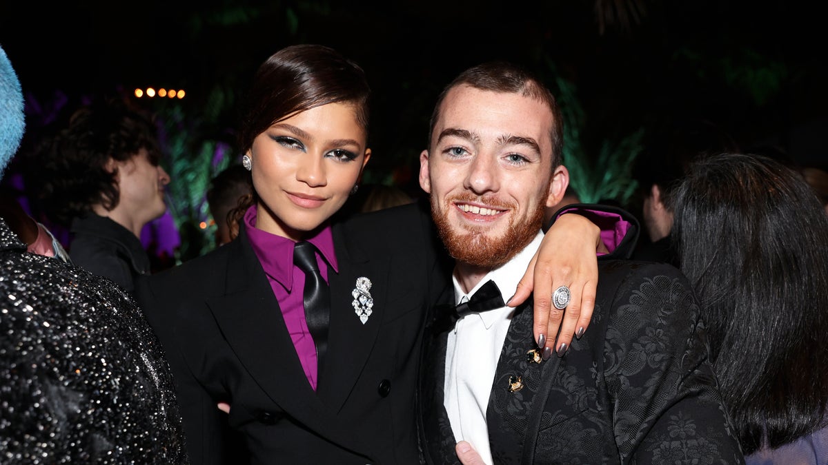 Zendaya in a purple shirt and black suit jacket posing with Angus Cloud wearing a black suit jacket and white shirt