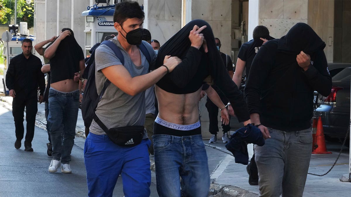 men cover their faces during police escort