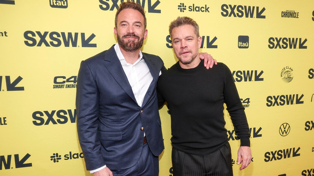 Ben Affleck em camisa branca e terno azul passa o braço em volta de Matt Damon vestindo uma camisa preta no SXSW