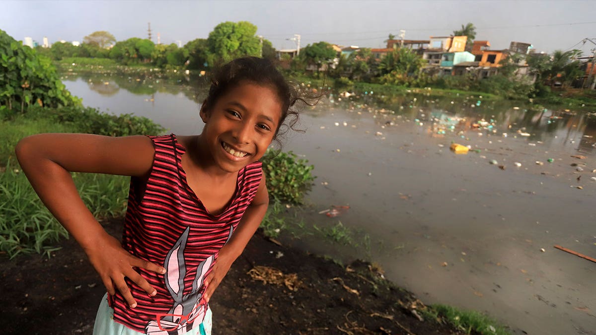 girl smiles near Brazilian river covered in litter