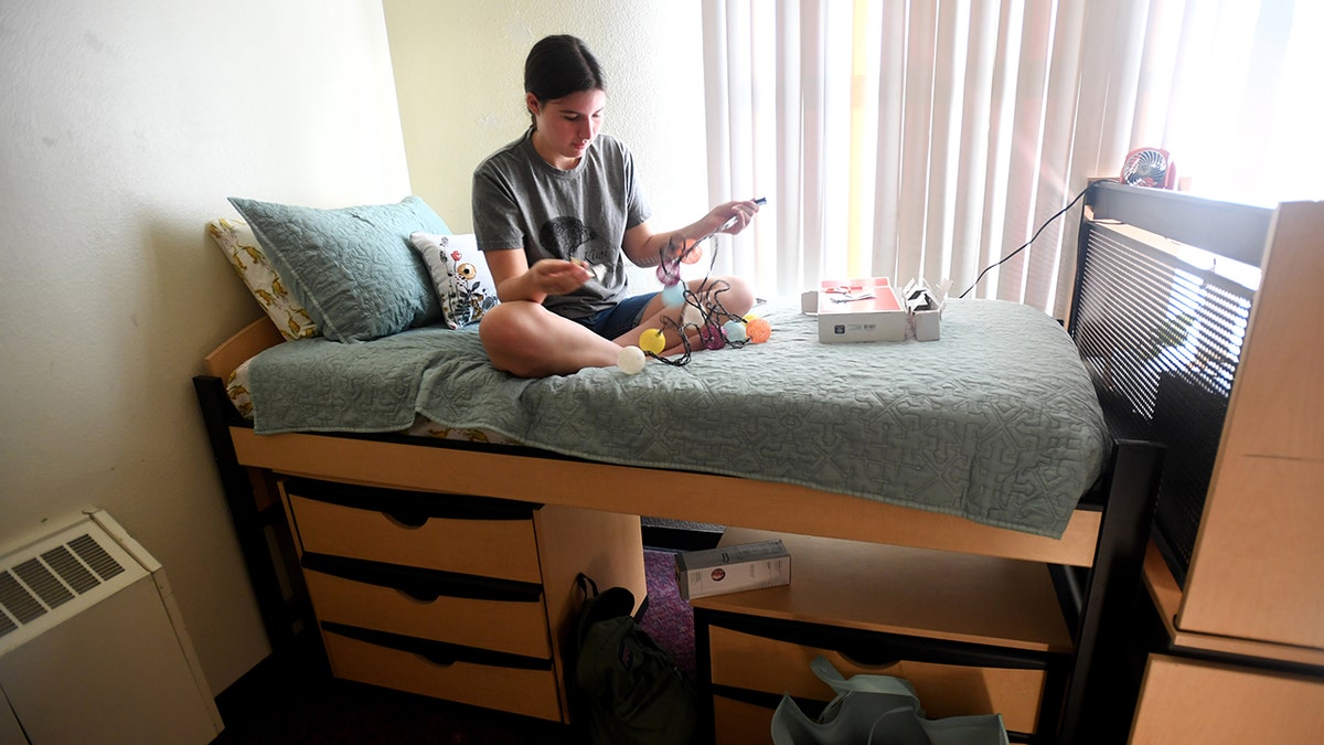 College student sitting on bed in dorm room
