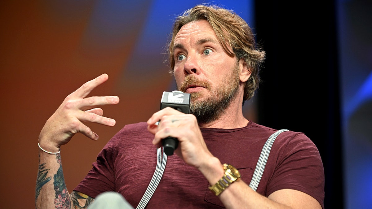 Dax Shepard, actor and podcaster, in marron shirt, holding microphone