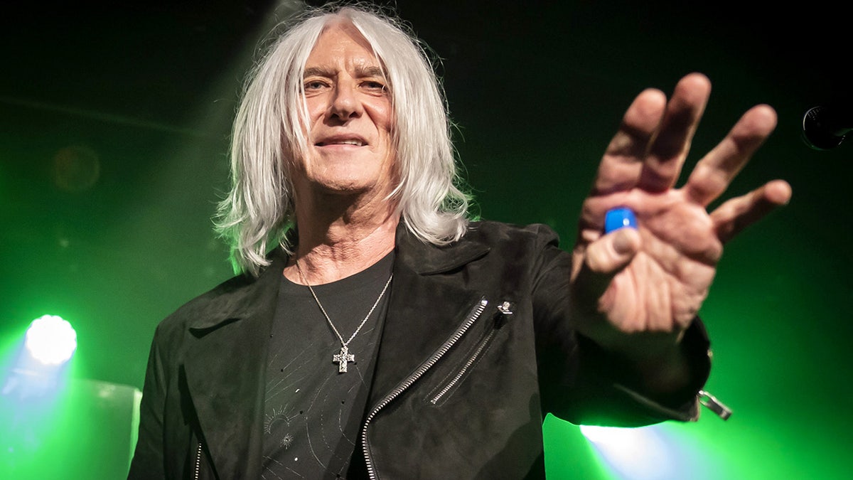 Joe Elliot reaches for the crowd in a black jacket with a cross necklace hanging around his neck