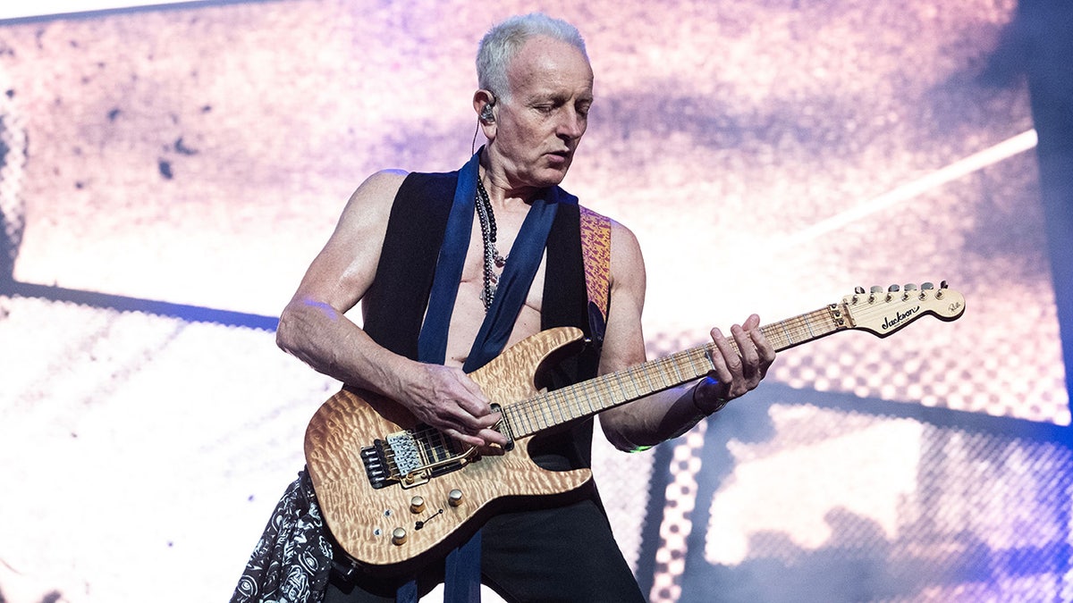 Phil Collen performs in Denmark, playing the electric guitar wearing an open vest, no shirt underneath and a loose navy tie