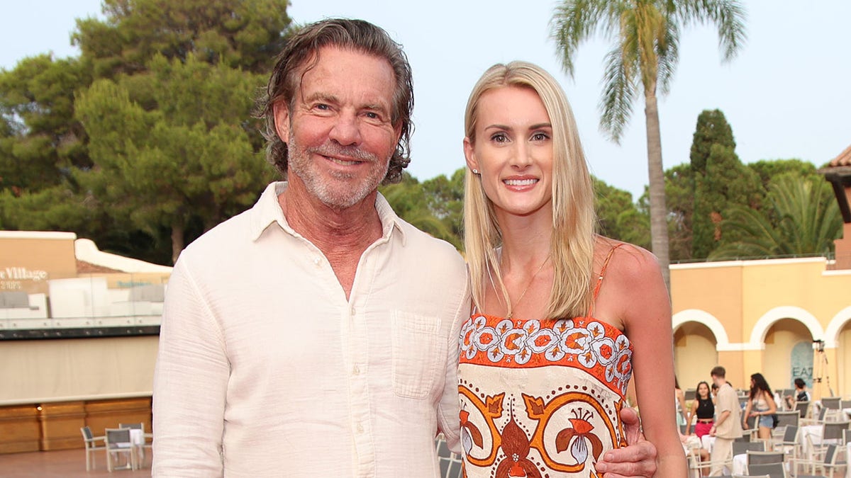 Dennis Quaid and wife Laua Savoie smile for portrait with palm tree in background