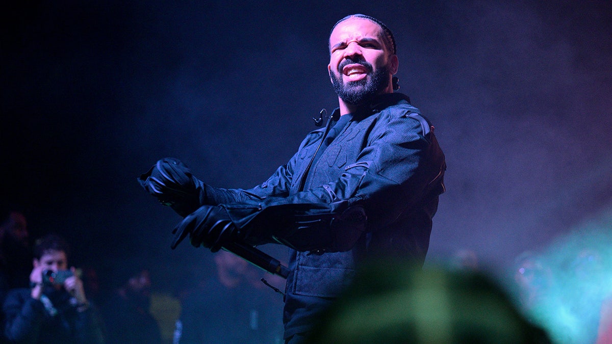 Drake in a black jacket and gloves performs on stage in Atlanta