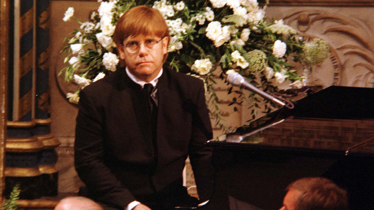 Elton John with red hair looks heartbroken at the piano during Princess Diana's funeral