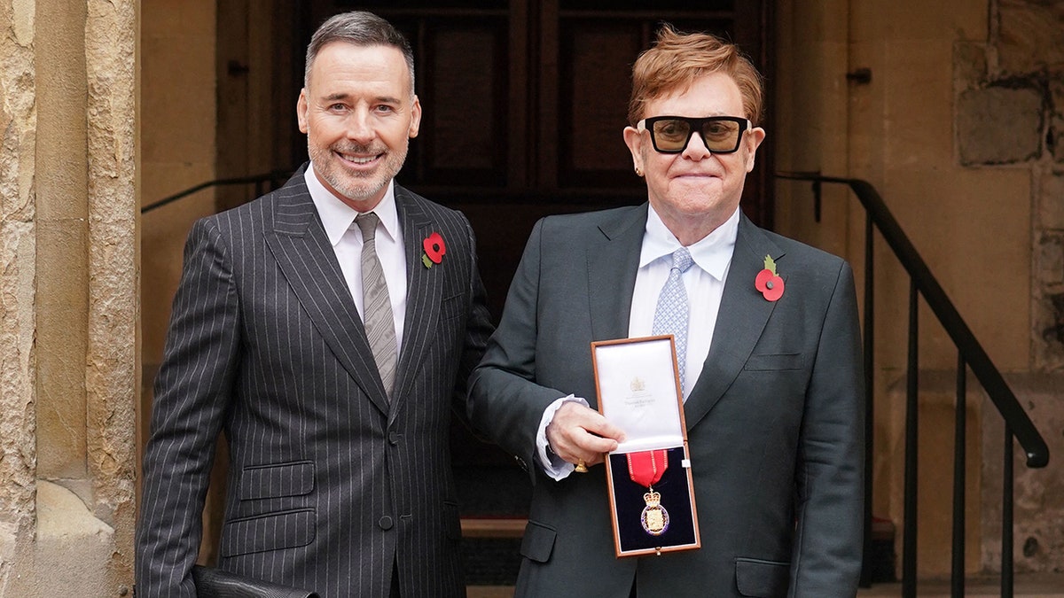 David Furnish poses next to Elton John who holds a medal in his right hand for being made a member of the Order of the Companions of Honour for services to Music and to Charity