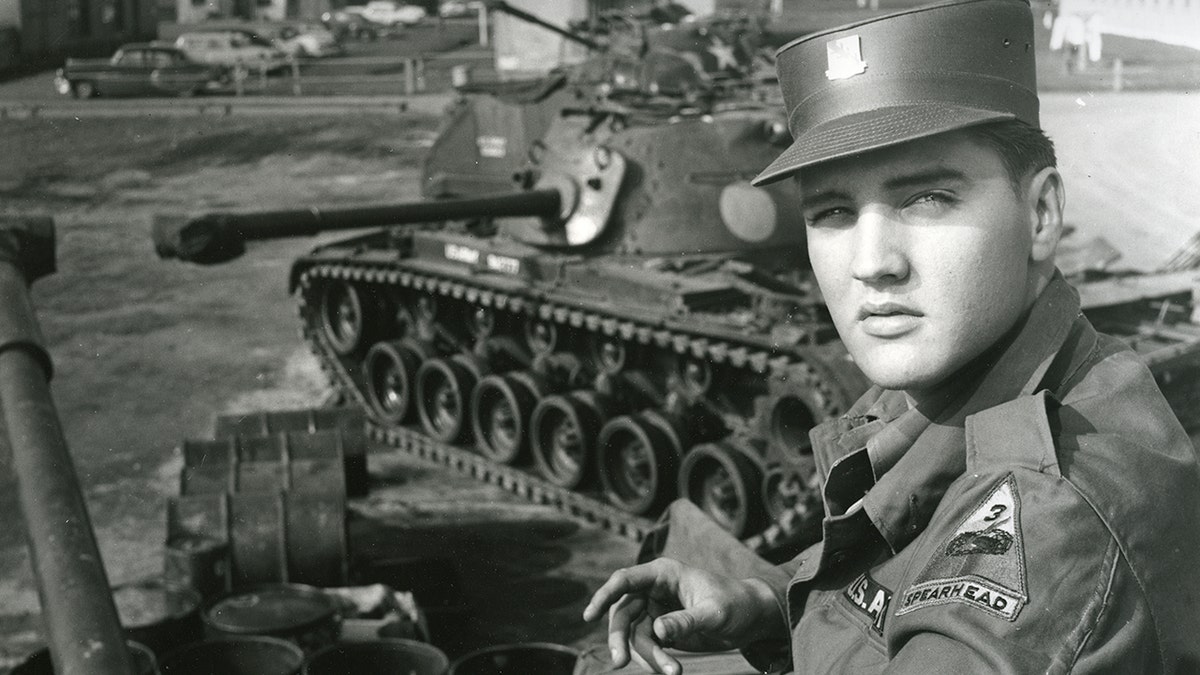 Elvis Presley poses for portrait by military tanks