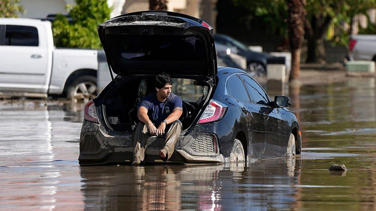 man waits in car stuck in flooded street