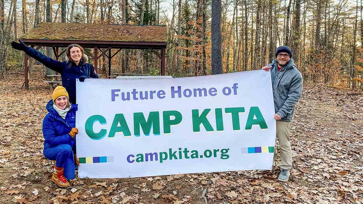 Sydney, Morgan, and Isaiah Mosher in fall clothing holding a sign stating "Future Home of CAMP KITA"