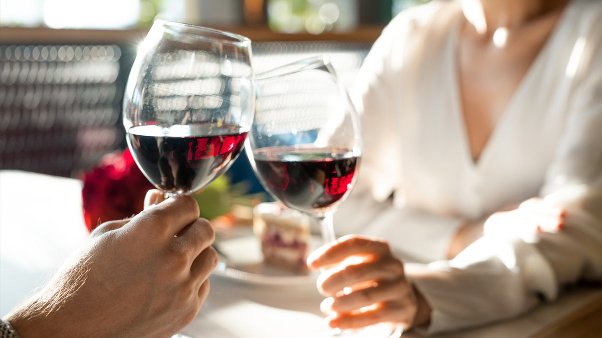 A man and woman toast glasses of red wine.