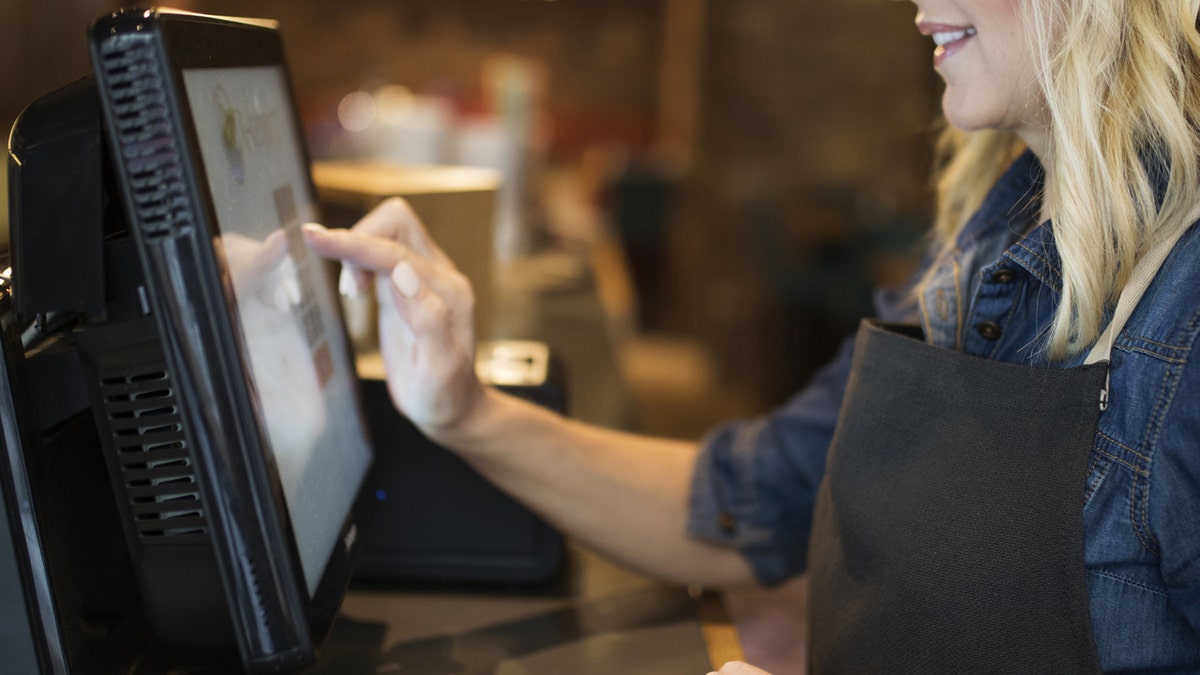A female server touches buttons on cash register screen.