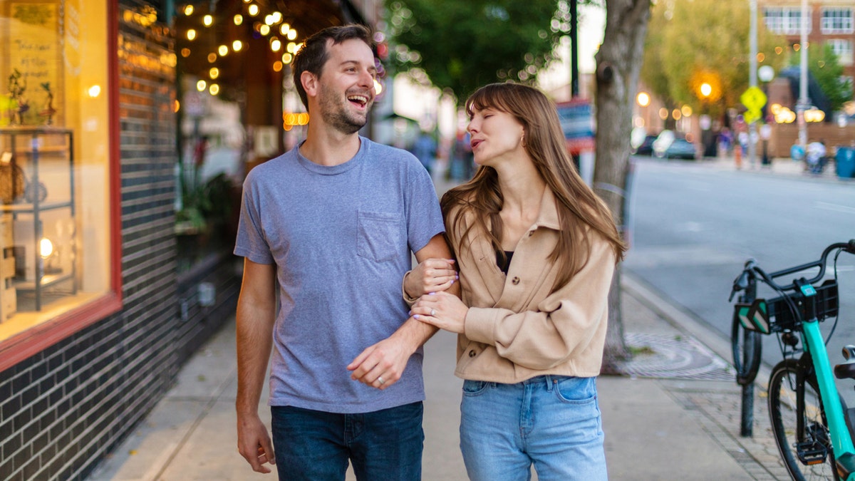 Couple with a visible height difference walks arm-in-arm down street.