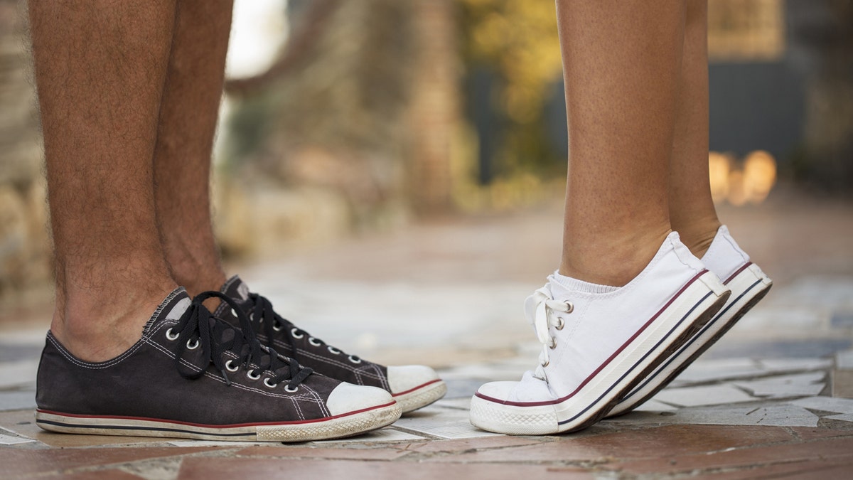 Close-up view of sneakers in which it appears a girl is getting on her tip toes to kiss a boy.