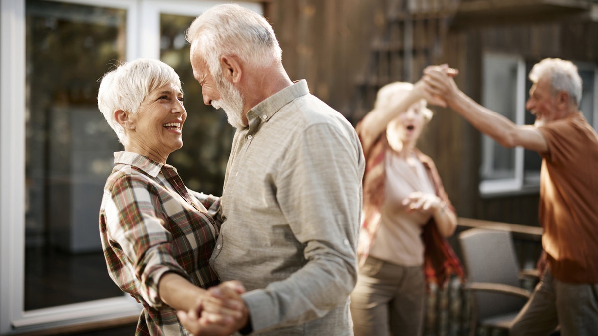Two senior couples with height differences dance at a gathering.