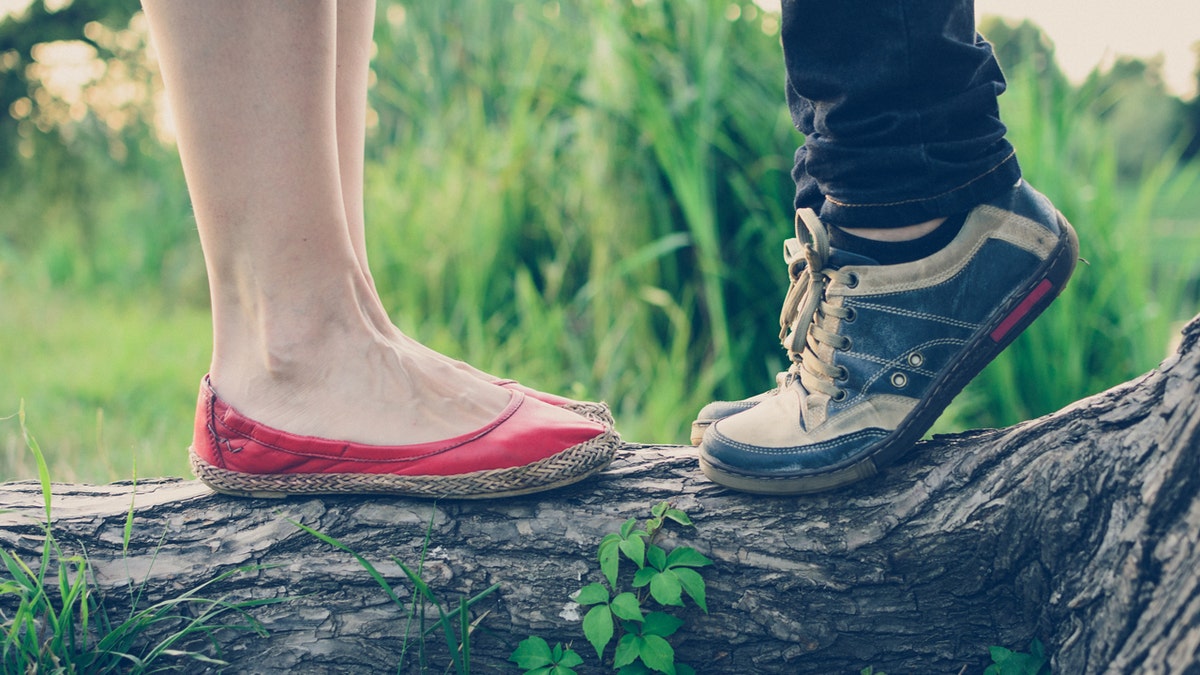 Close-up view of shoes in which it appears a boy is getting on his tip toes to kiss a girl.