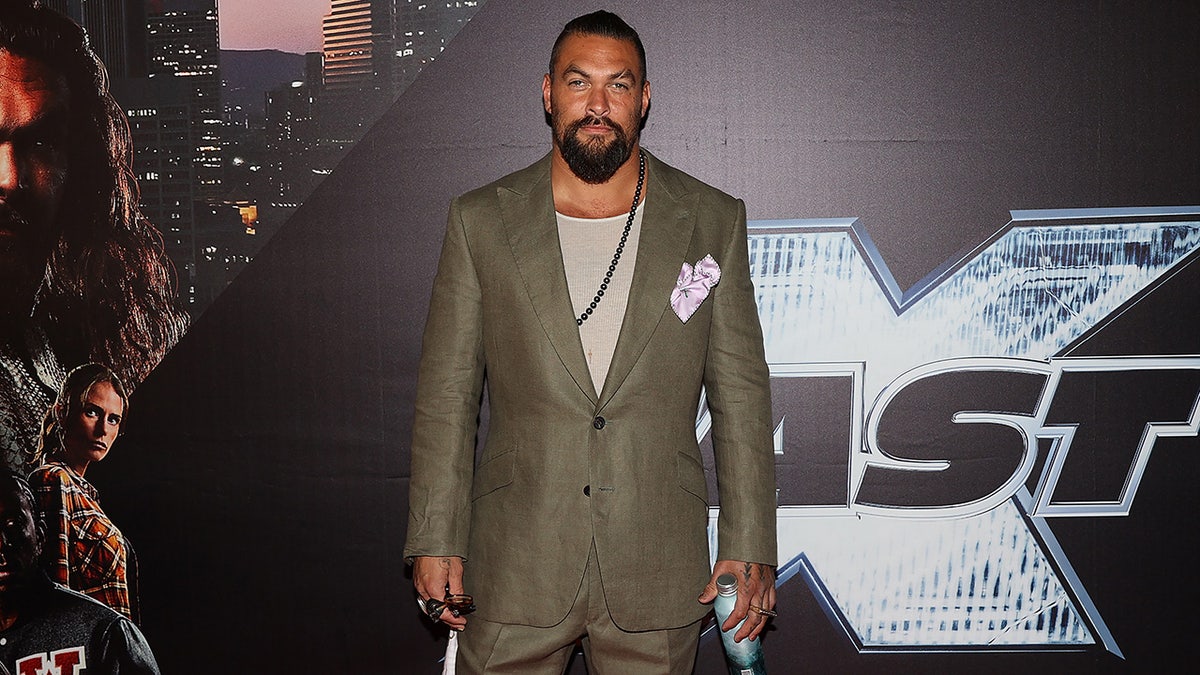 Jason Momoa in a green suit with a chain necklace on the carpet in Auckland, New Zealand