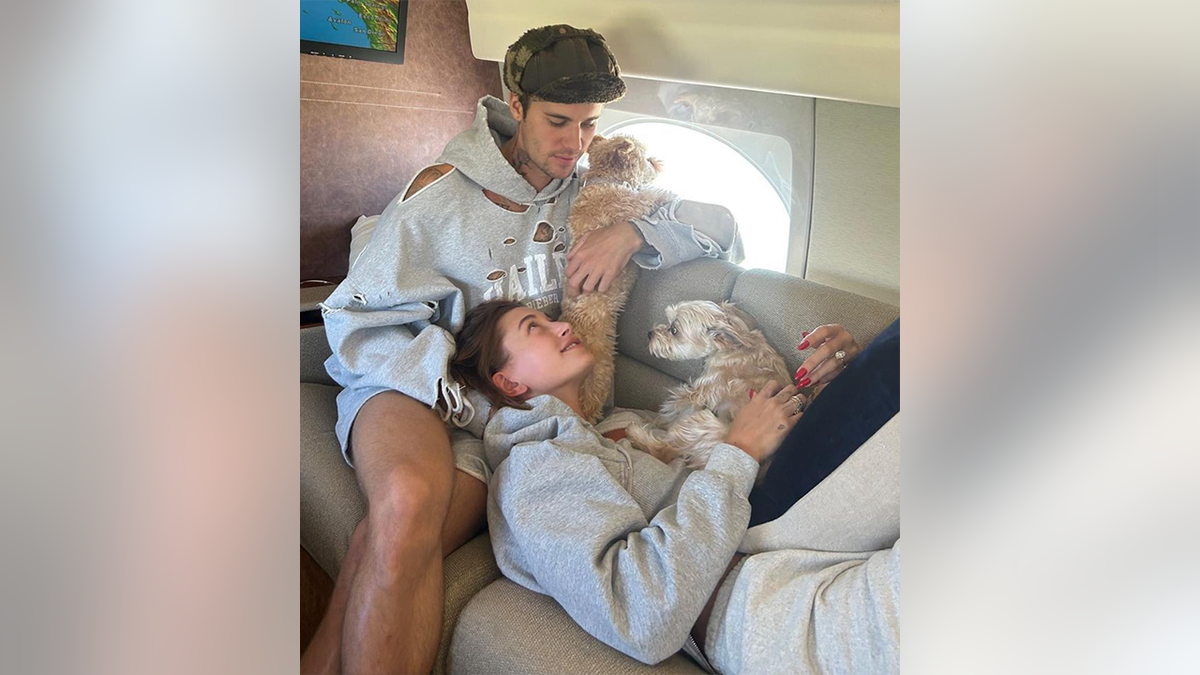 Justin Bieber looks down at Hailey Bieber wearing a sweatshirt that has her name on it and their two dogs on a private jet