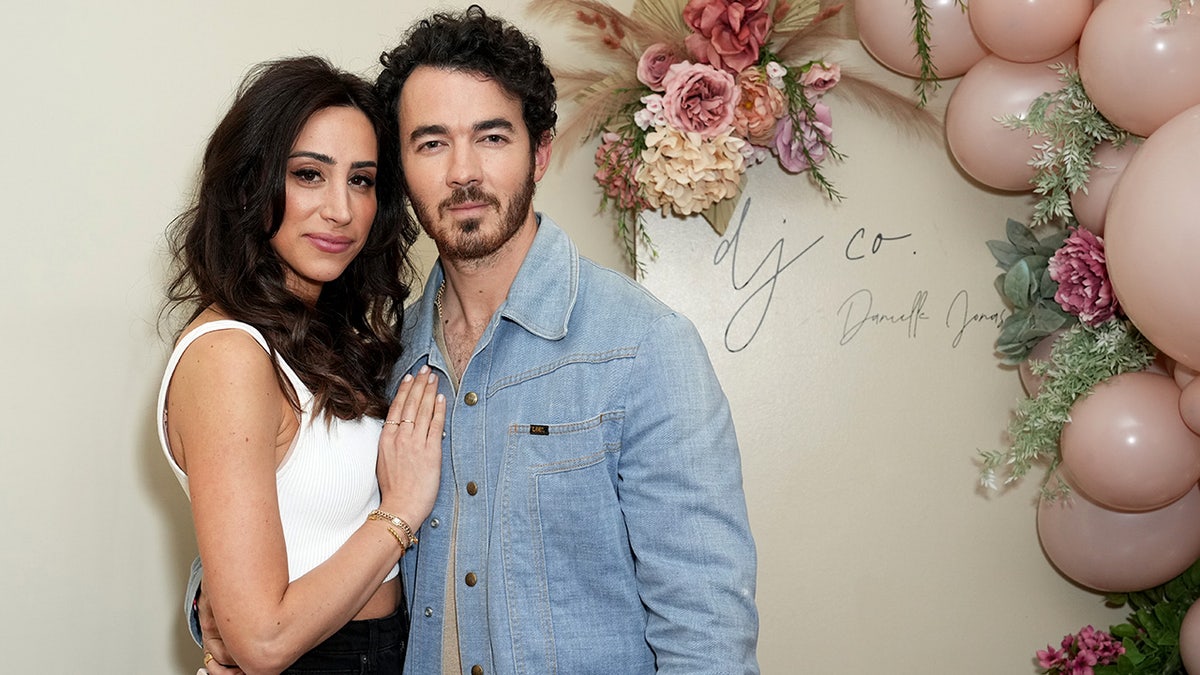 Danielle Jonas in a white tank top places her hand on her husband Kevin Jonas' chest, he's wearing a jean jacket at a boutique