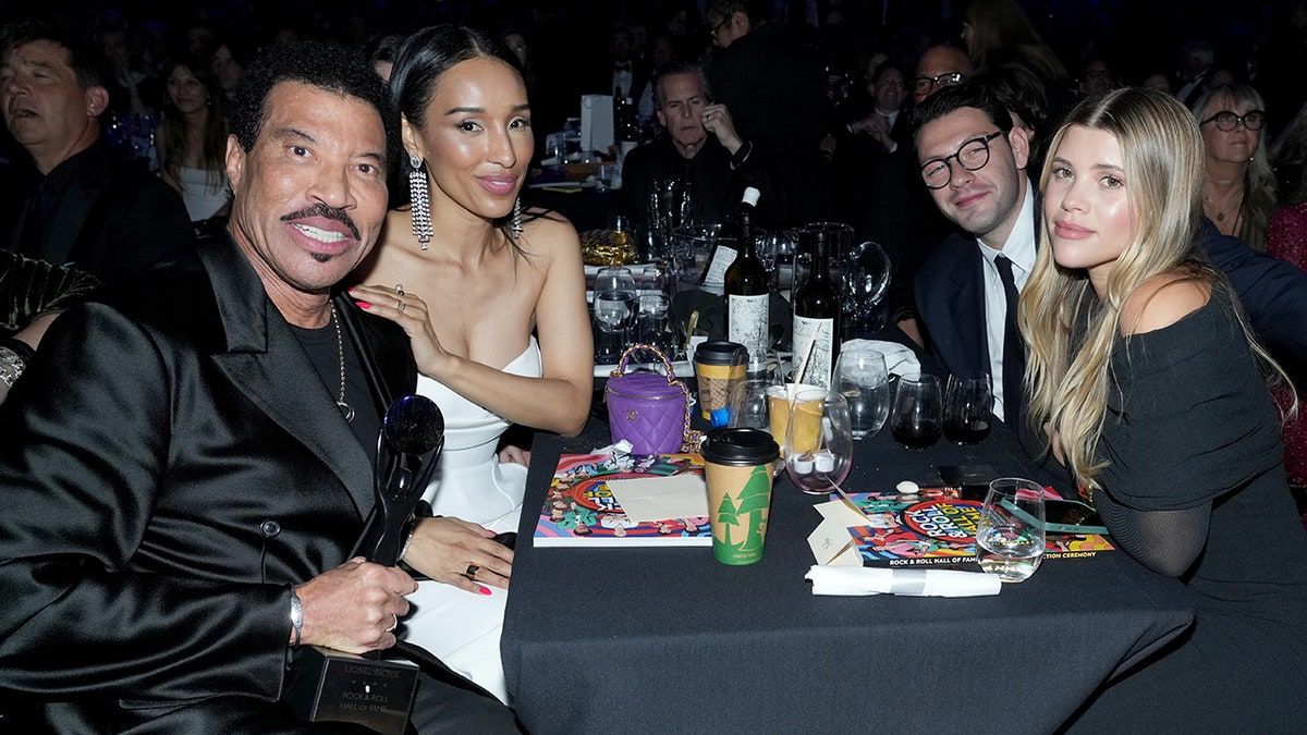 Lionel Richie at the Rock & Roll Hall of Fame ceremony with his girlfriend Lisa Parigi in a white dress and they sit across from Sofia Richie and her now-husband Elliot Grainge