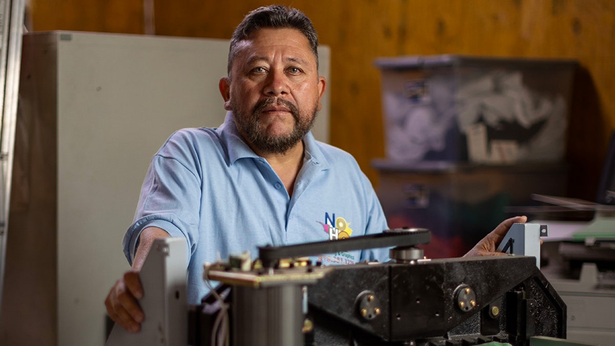 Shop owner stands behind large printing machine