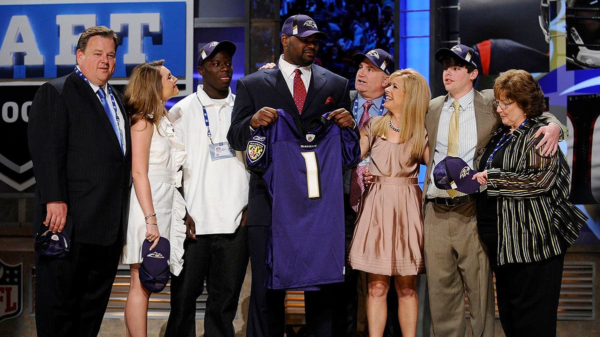 Michael Oher holds a Baltimore Ravens jersey on stage and poses with his family including the Tuohy's on stage