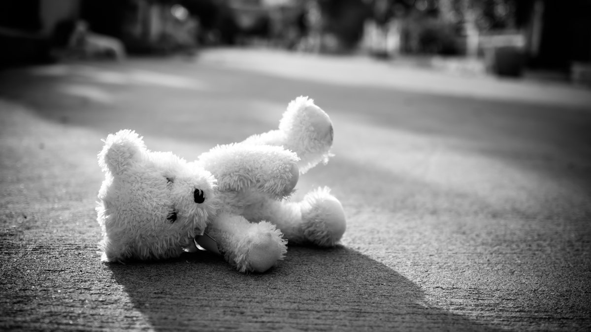 Stuffed bear lies on the ground in black and white photo