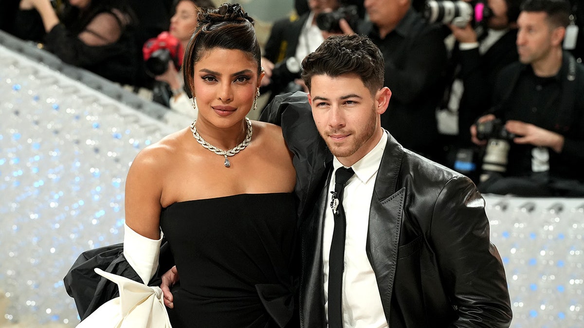 Priyanka Chopra in a black gown and updo smiles on the Met Gala carpet with husband Nick Jonas in a leather black suit