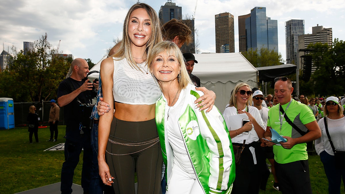 Chloe Lattanzi in a crop top and leggings holds on to her mother Olivia Newton-John in a white and green jacket at the Olivia Newton-John Wellness Walk and Research run in 2019