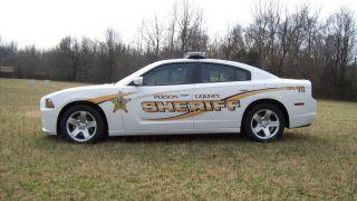 Police car in grass, woods behind it