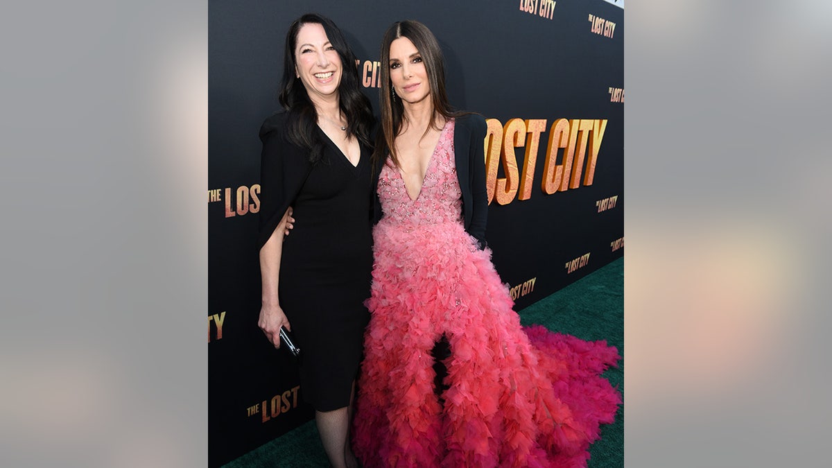 Gasine Bullock-Prada in a black dress smiles on the red carpet next to sister Sandra Bullock in a beautiful pink dress with a feather train on the carpet for the premiere of "The Lost City"