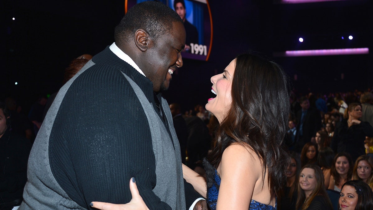 Quinton Aaron looks down at Sandra Bullock as she grabs his arms and laughs upward at the People's Choice Awards