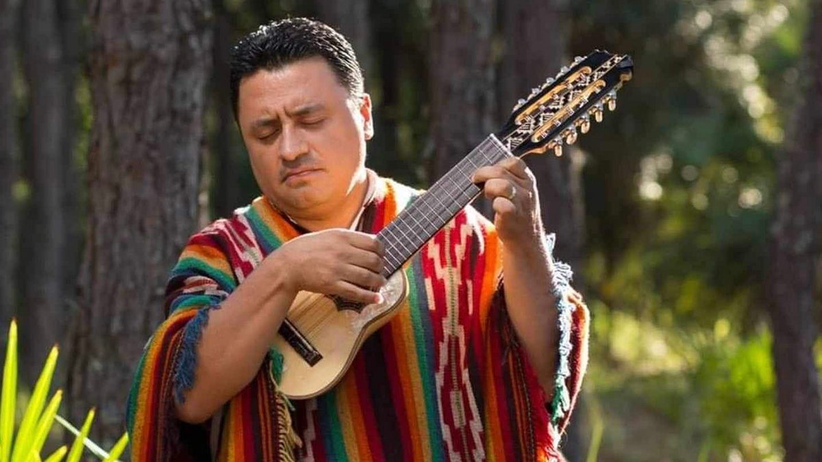 man in poncho playing small guitar
