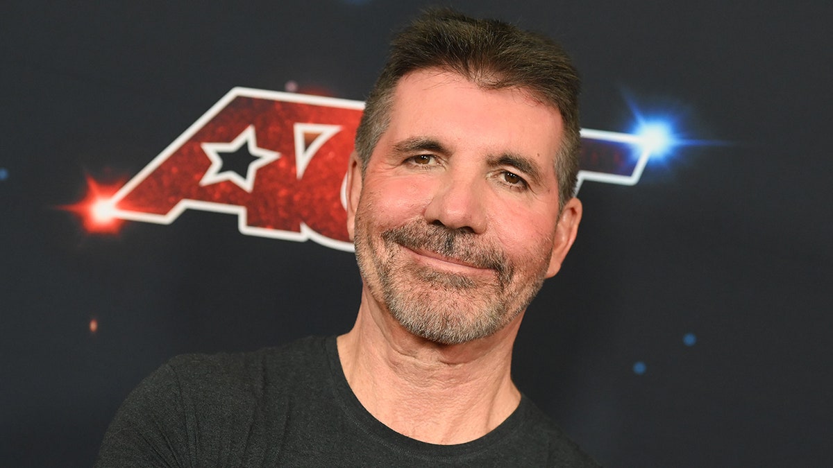 Simon Cowell smirks on he "AGT" carpet in a black scoop neck shirt