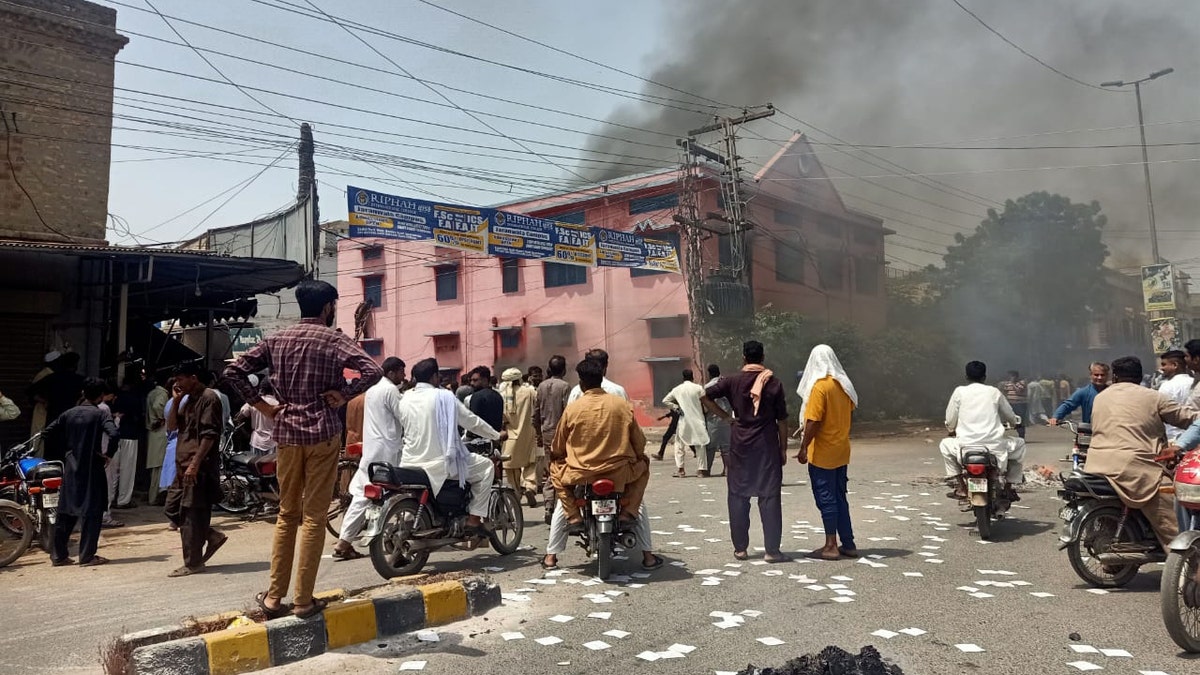People stand on the street and watch as smoke rises from a burning church in Pakistan