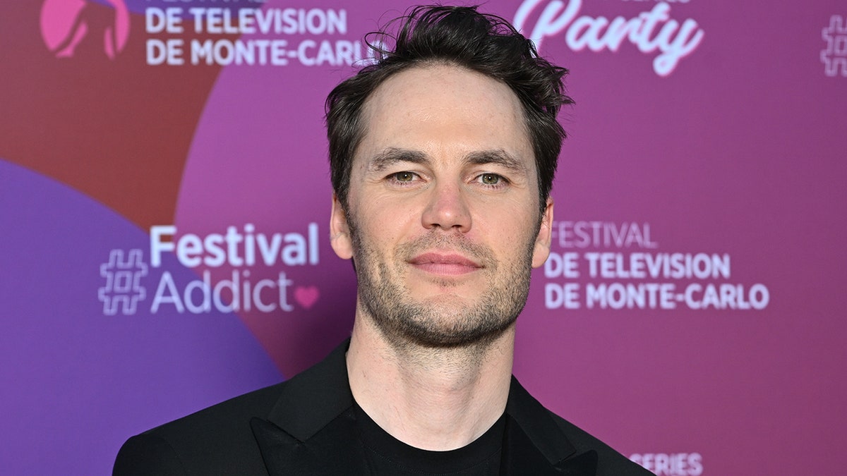Taylor Kitsch tilts his head up a little and soft smiles wearing black in Monte-Carlo