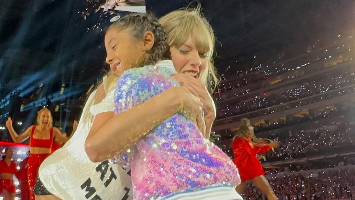 Taylor Swift in a t-shirt for her "Red" era during The Eras Tour hugs Bianka Bryant in a sparkly jacket
