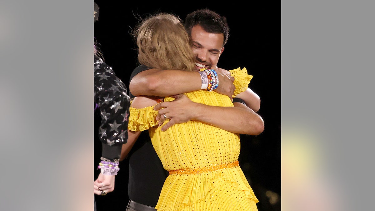 Taylor Swift in a yellow dress gives a beaming Taylor Lautner a hug on stage