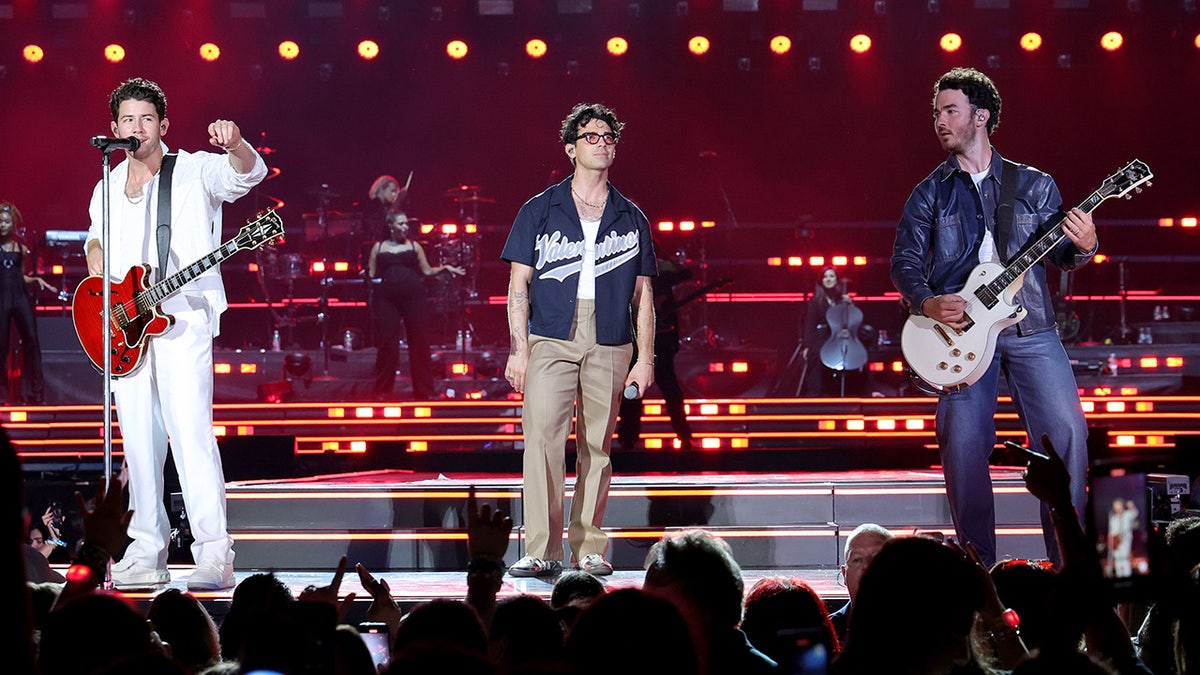 Nick in all white, Joe Jonas in a jersey and Kevin in a blue jacket perform at Yankee Stadium for opening night of "The Tour"