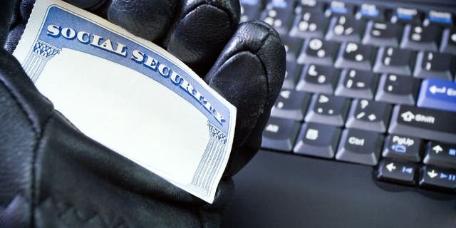 Picture of a cybercriminal holding a social security card in one hand while wearing a black glove and by a computer keyboard