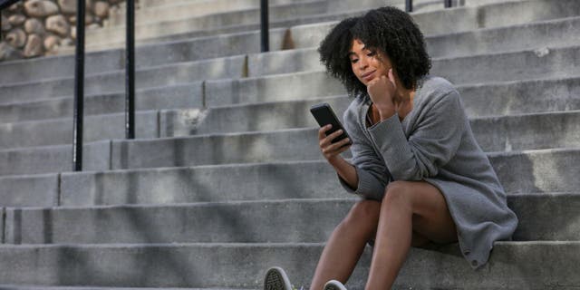 Woman sits on building steps and holds her phone