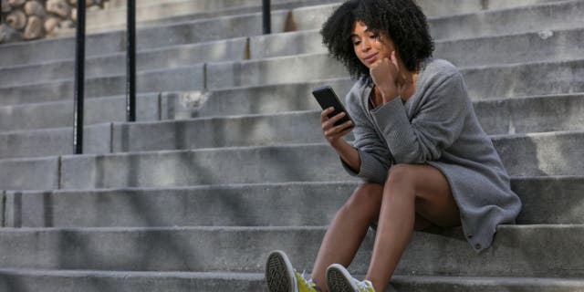 Woman sits on building steps and holds her phone