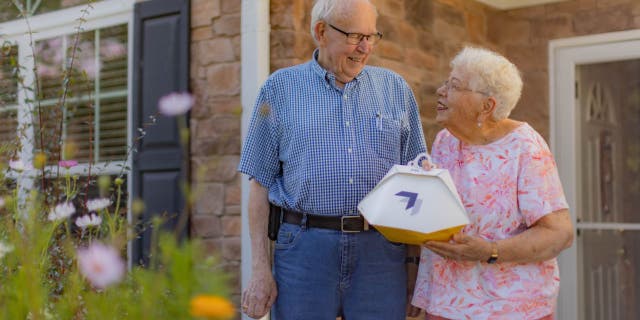 Elderly couple Paul and Susie Sensmeier outside their home, Susie is holding the Wing delivery order