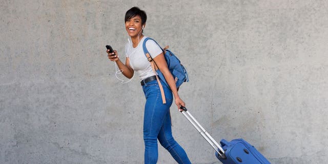 Woman walking with her phone and luggage.
